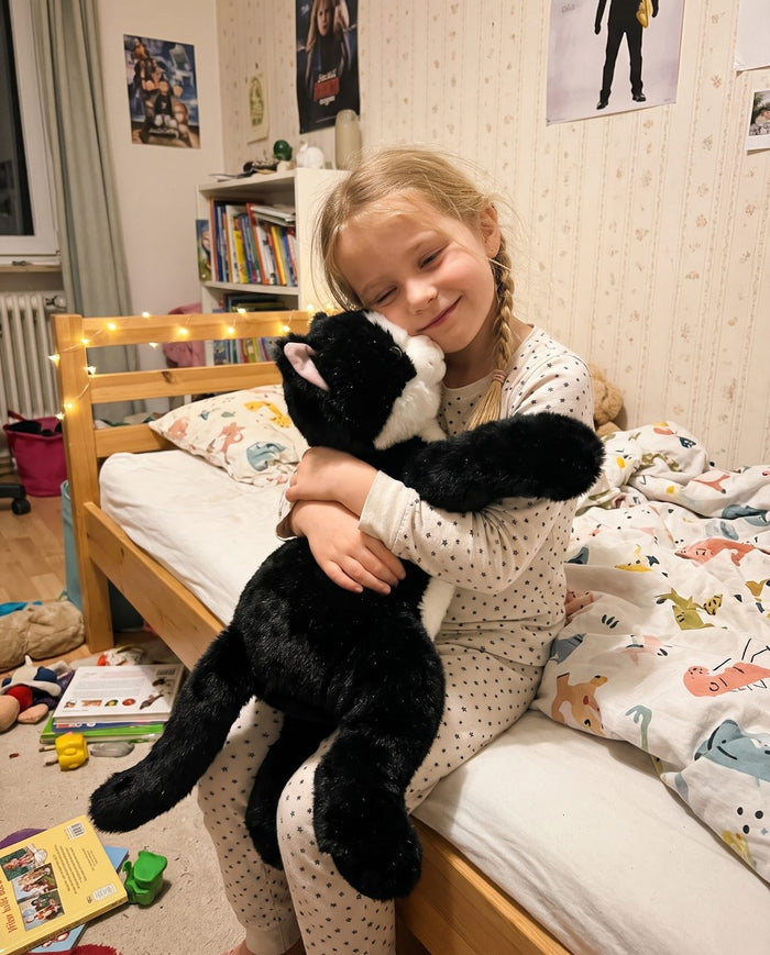 Mädchen mit Zöpfen umarmt das Katzen-Gewichtskuscheltier im Kinderzimmer