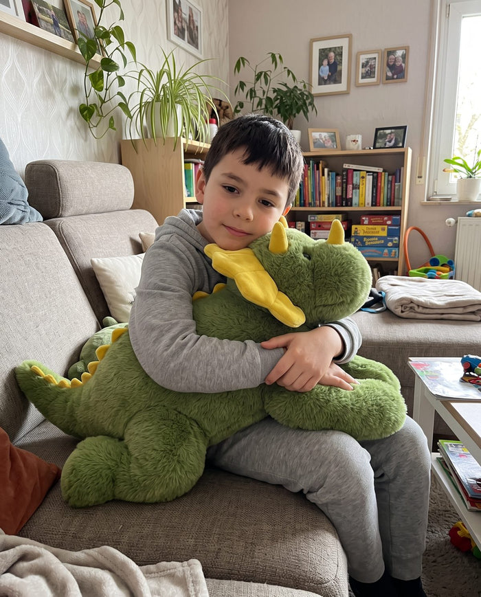 Junge auf dem Sofa umarmt das Dino-Gewichtskuscheltier