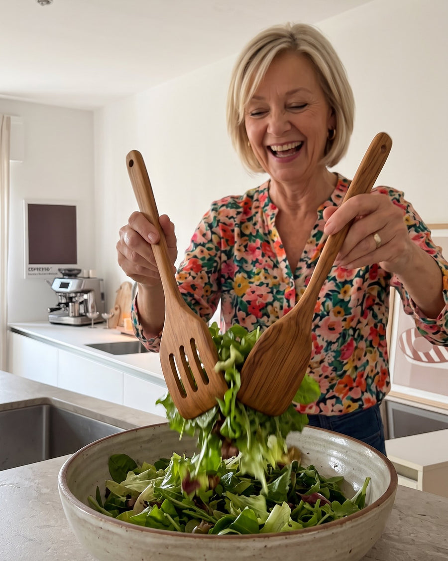 Frau mischt Salat mit zwei Teak-Helfern