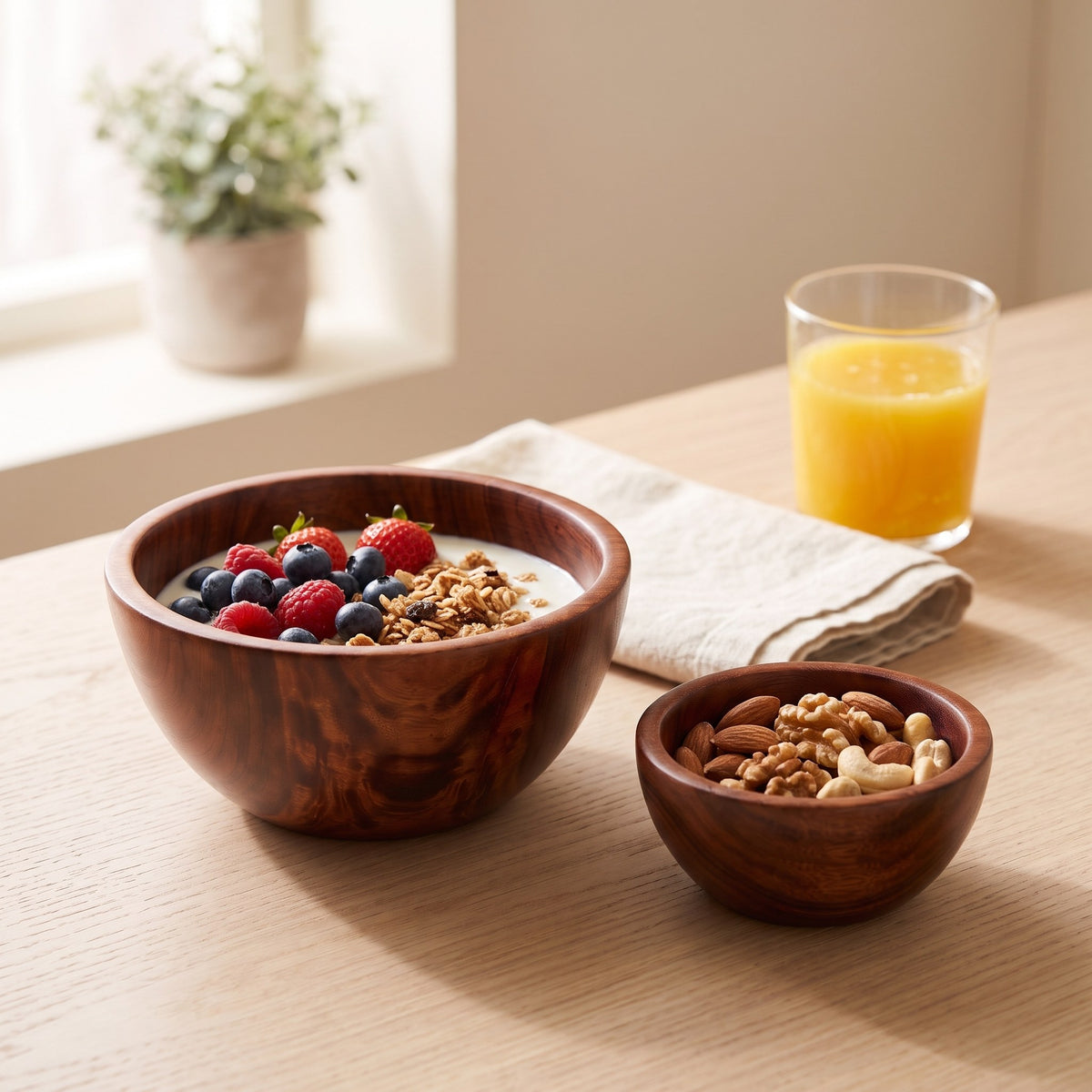 Jujube-Holzschale mit Joghurt, Beeren und Nüssen, daneben eine kleine Schale mit Nüssen und ein Glas Orangensaft